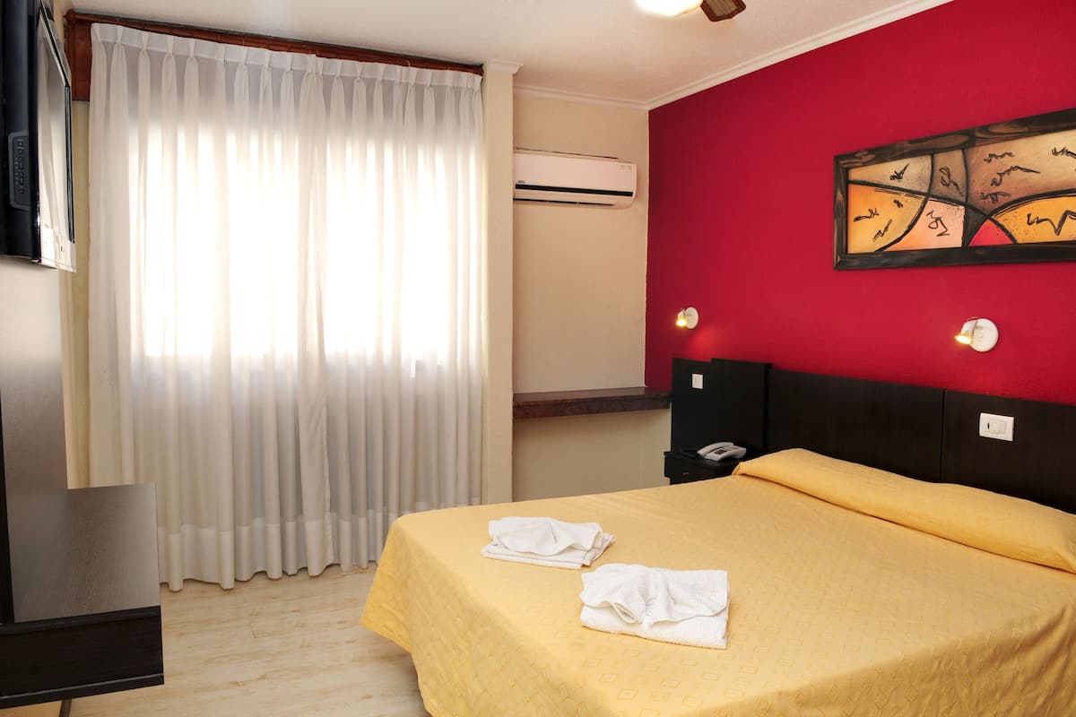 Une chambre d’hôtel avec un lit, une télévision, un appareil de climatisation et un mur d’accent de couleur rouge.