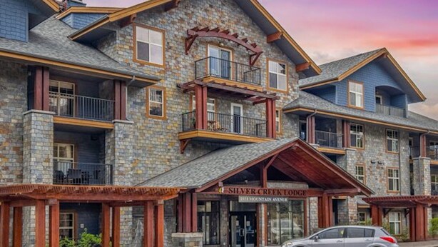 Una cabaña de varios pisos con fachada de piedra y balcones de madera, llamada "Silver Creek Lodge".
