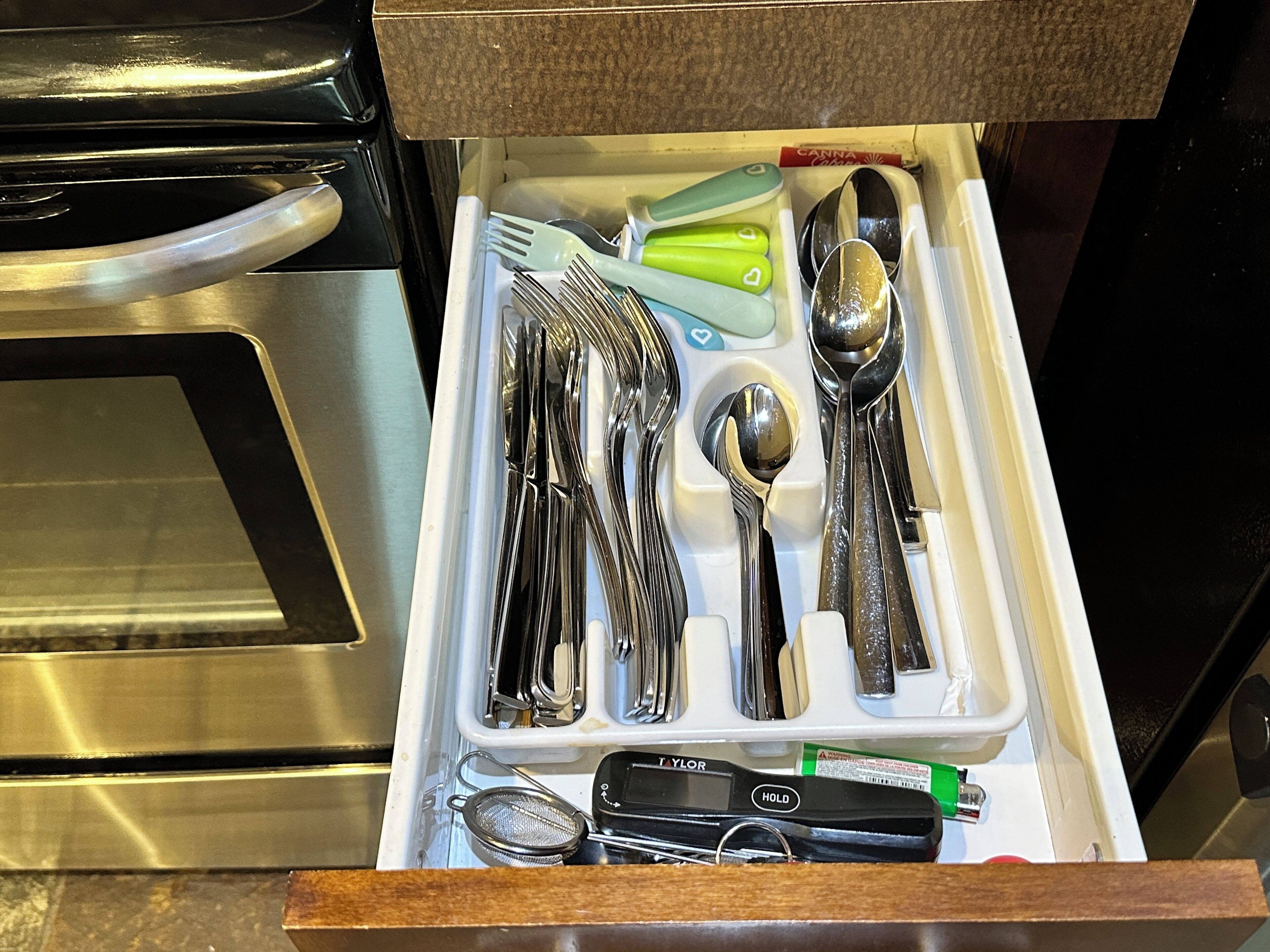 A drawer containing various kitchen utensils including forks, spoons, and a strainer.
