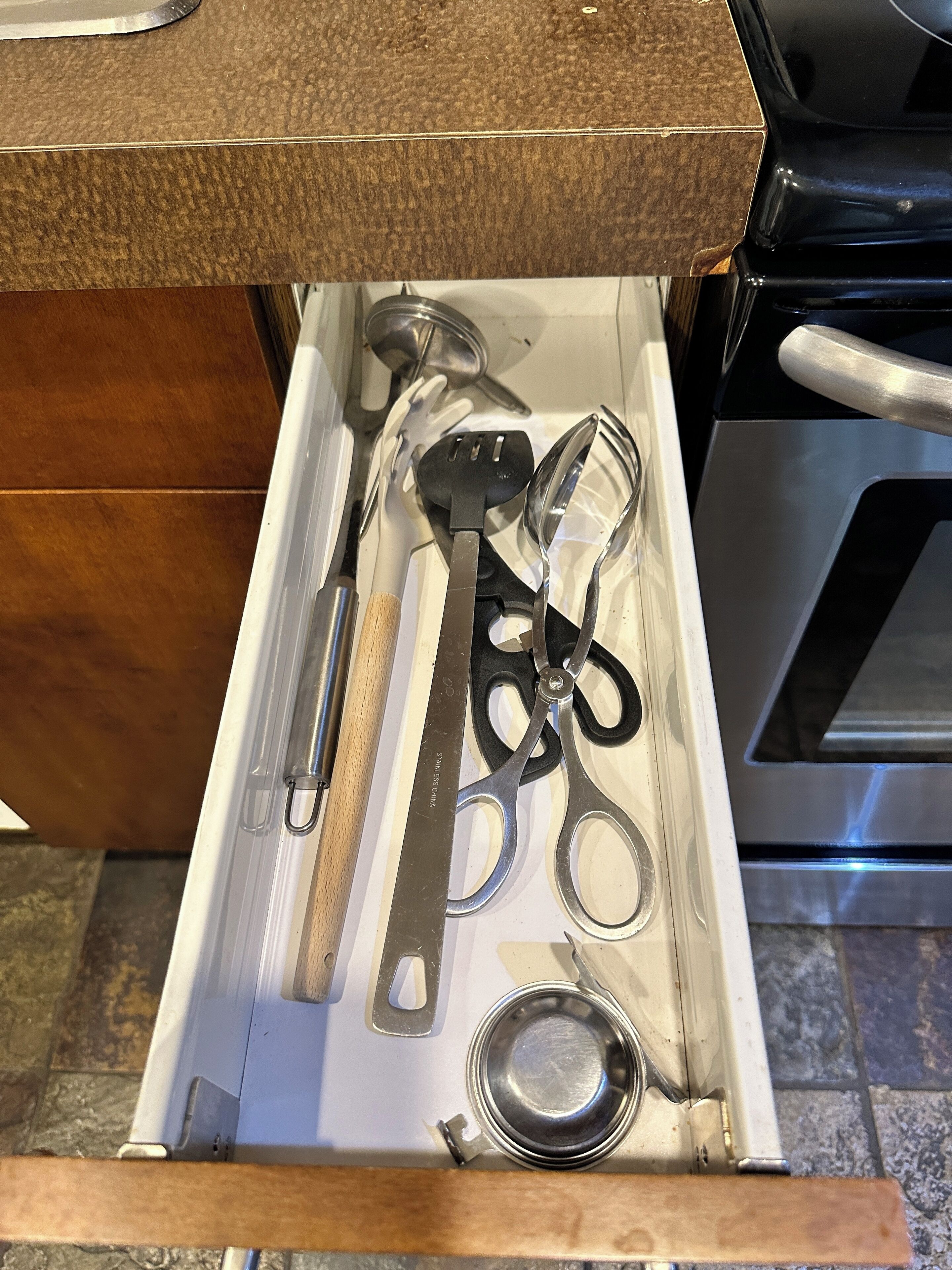 Un tiroir de cuisine contenant divers ustensiles, notamment une spatule, des pinces et une paire de ciseaux.