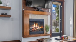 Una sala de estar con chimenea, un televisor montado encima y una puerta que da a un balcón.