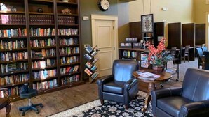 A library with bookshelves, leather chairs, a clock, and a door.