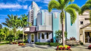 A modern hotel with a theater, palm trees, and a well-maintained garden.