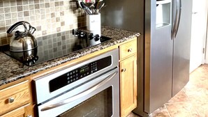 A kitchen with wooden cabinets, stainless steel appliances including a microwave, oven, and refrigerator, a granite countertop, and a tiled backsplash. - Golf Cart to Beach, Pet Friendly, Fenced Yard, Amelia Island Quiet Home Escape (Fernandina Beach)