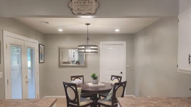 A dining area with a round table, four chairs, a chandelier, and a kitchen visible through an open door. - Traveller's peaceful paradise (Muskogee)