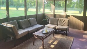 A covered patio area with two sofas and a small table, large windows, and a view of a grassy yard. - Traveller's peaceful paradise (Muskogee)