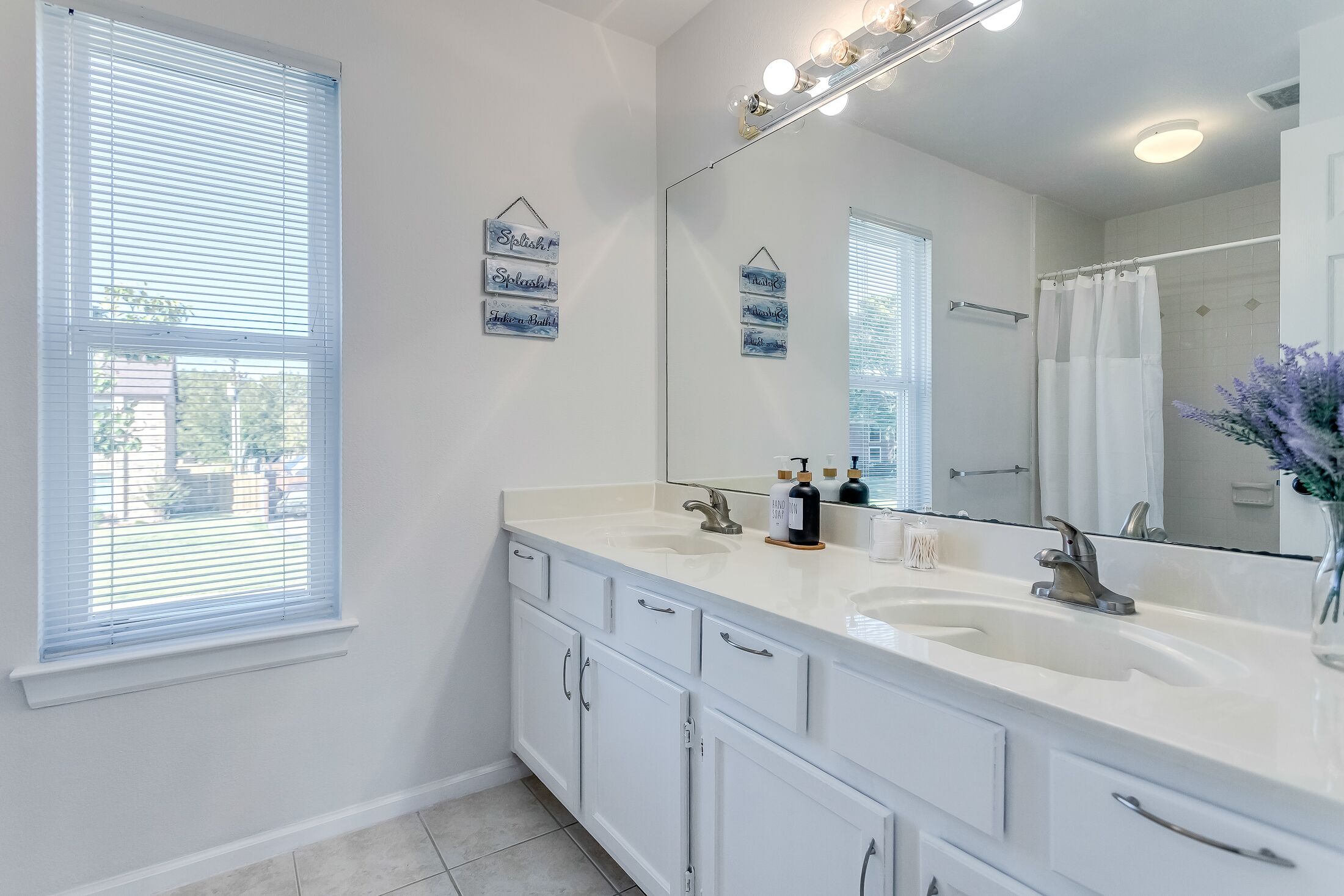 A bathroom with two sinks, a large mirror, and a shower curtain.