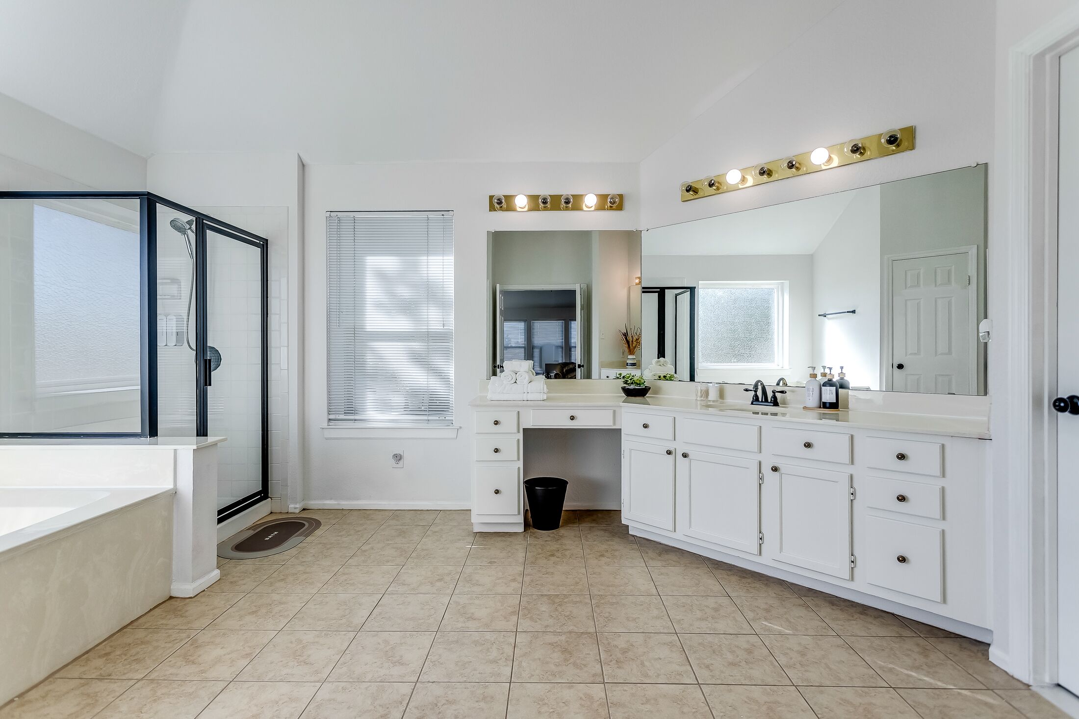 A modern bathroom with a walk-in shower, a vanity with a large mirror and lights, and a toilet.