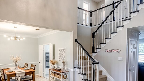 A spacious dining area with a wooden table and chairs, a chandelier, and a staircase with a "WELCOME" sign.