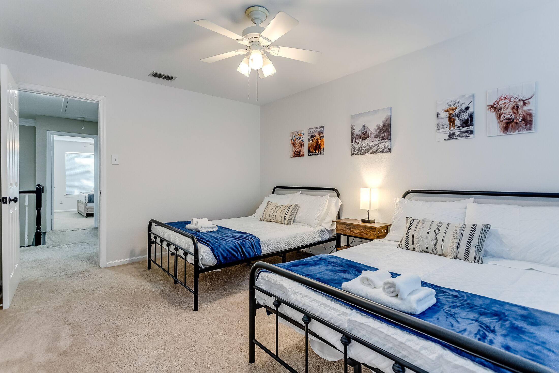 A bedroom with two beds, a ceiling fan, and artwork on the walls.