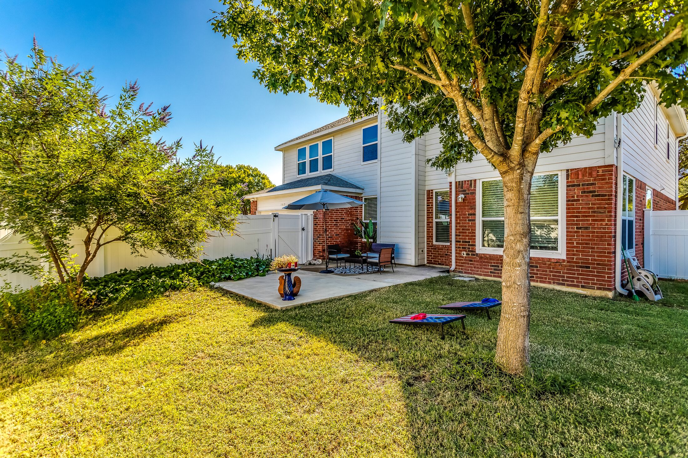 A two-story house with a patio, a tree, and a small garden.