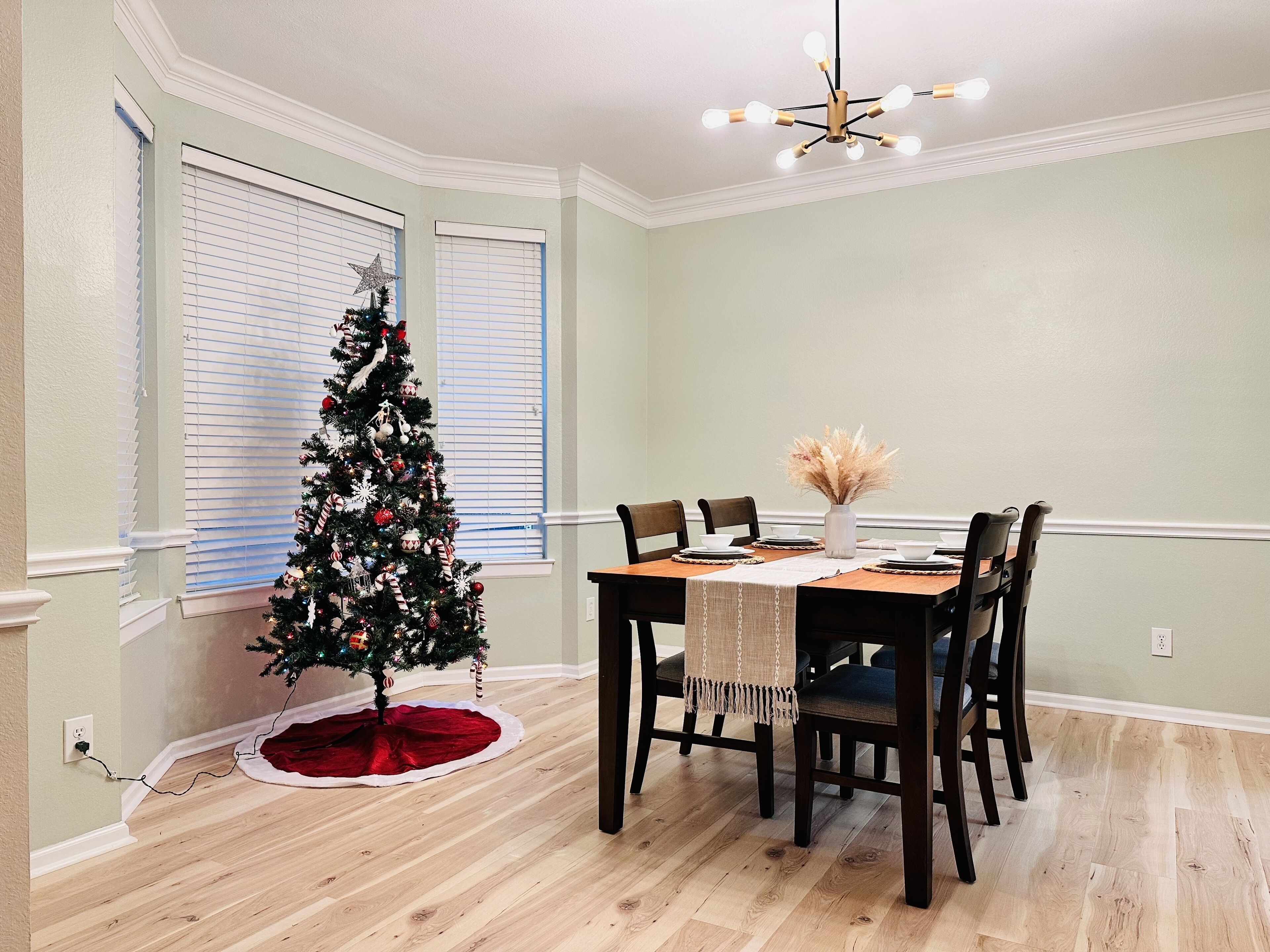 A dining area with a Christmas tree, a chandelier, and a table set for four.