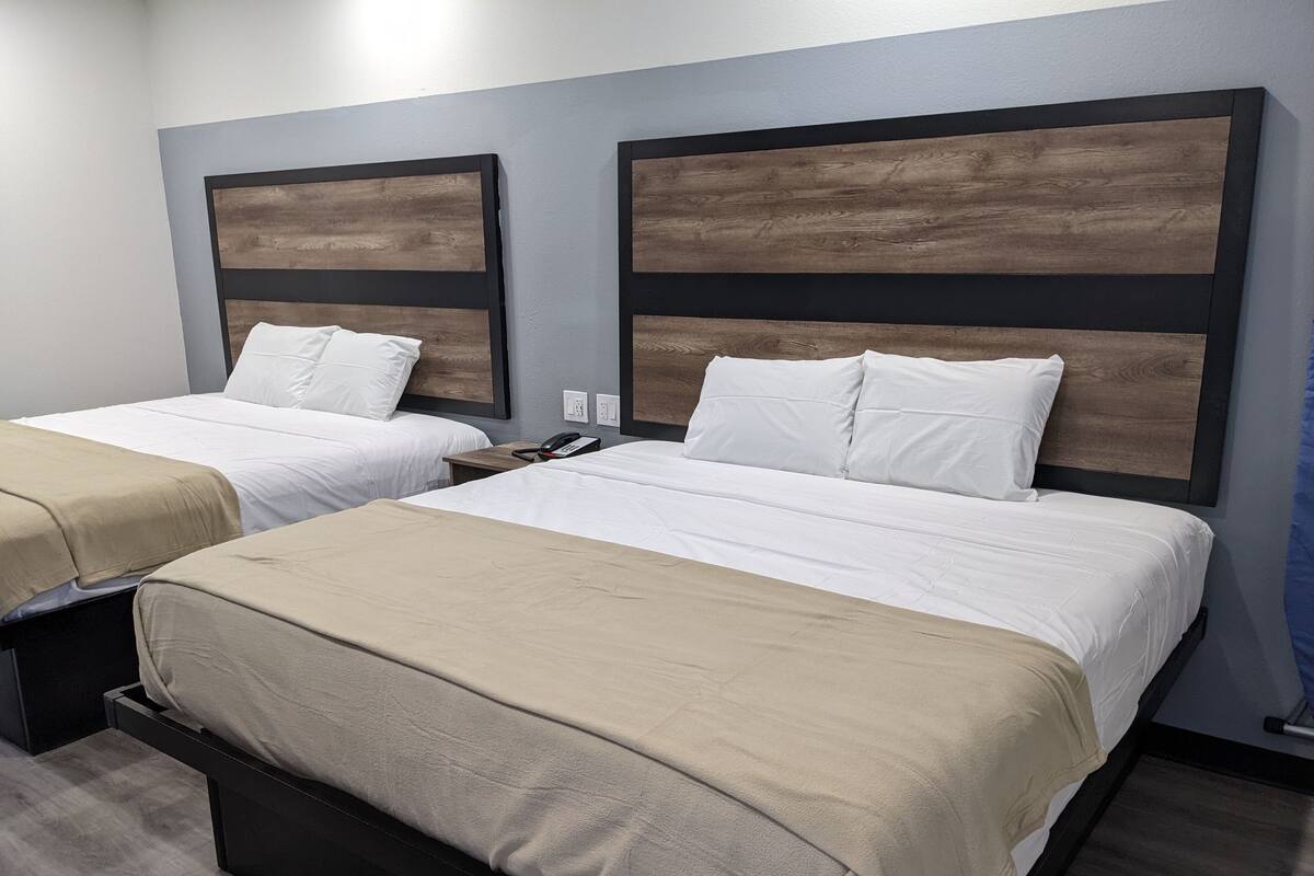 A hotel room with two beds, each with a wooden headboard, white bedding, and a beige throw blanket.