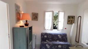 A small, cozy room with a sofa, a table, a cabinet, and a window with curtains. - Maison Petit Jardin au Calme Parking (Afa)