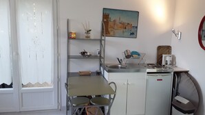 A compact kitchen with a dining table, a sink, and a small trash bin. - Maison Petit Jardin au Calme Parking (Afa)