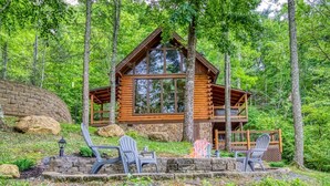 Une cabane en rondins avec des fondations en pierre, une terrasse avec des chaises et un foyer extérieur.