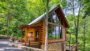 Une cabane en rondins dotée d’une véranda, de fondations en pierre et offrant une vue sur la forêt.