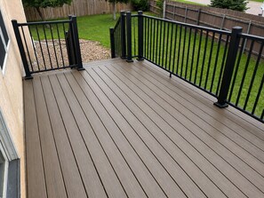 A wooden deck with black railings, a grassy yard, and a wooden fence in the background.