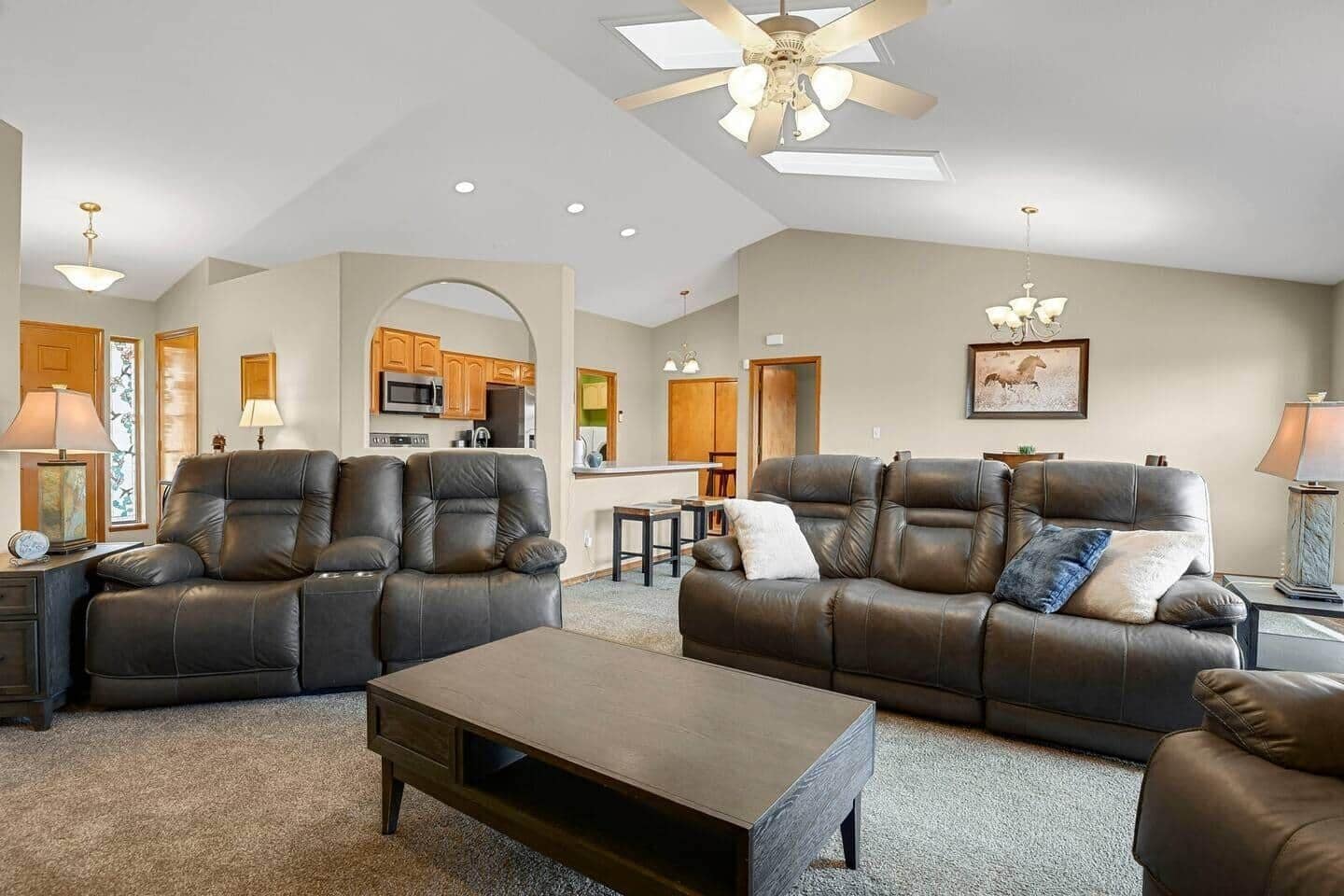 A spacious living room with two leather sofas, a coffee table, and a ceiling fan.
