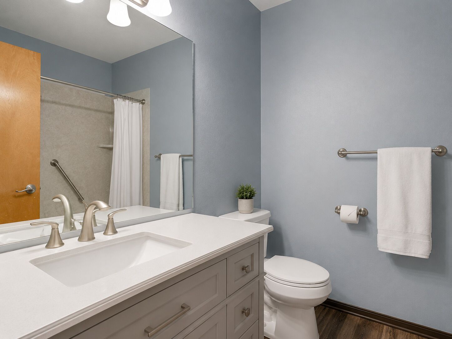A bathroom with a white sink, two faucets, a mirror, a toilet, a towel rack, and a small plant.