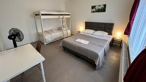 A bedroom with bunk beds, a desk, a chair, a fan, a heater, and a window with curtains.