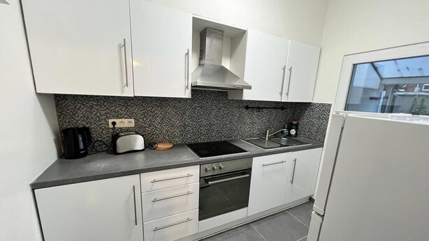A modern kitchen with white cabinets, a built-in oven, a stovetop, and a window.