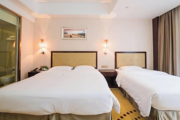 Habitación de hotel con dos camas, una mesita de noche, un cuadro en la pared y una ventana con cortinas.