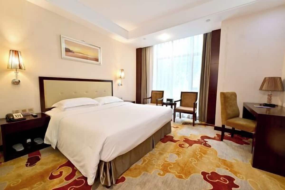 A hotel room with a large bed, a desk, a chair, and a small table.