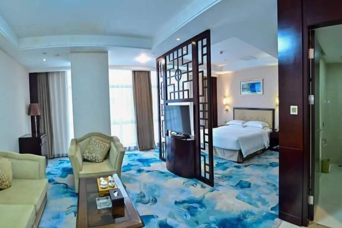 A hotel room with a bed, a sofa, a coffee table, and a decorative screen.