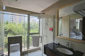Une salle de bain moderne avec une douche à l’italienne en verre, un grand miroir et une vue sur la verdure à l’extérieur.
