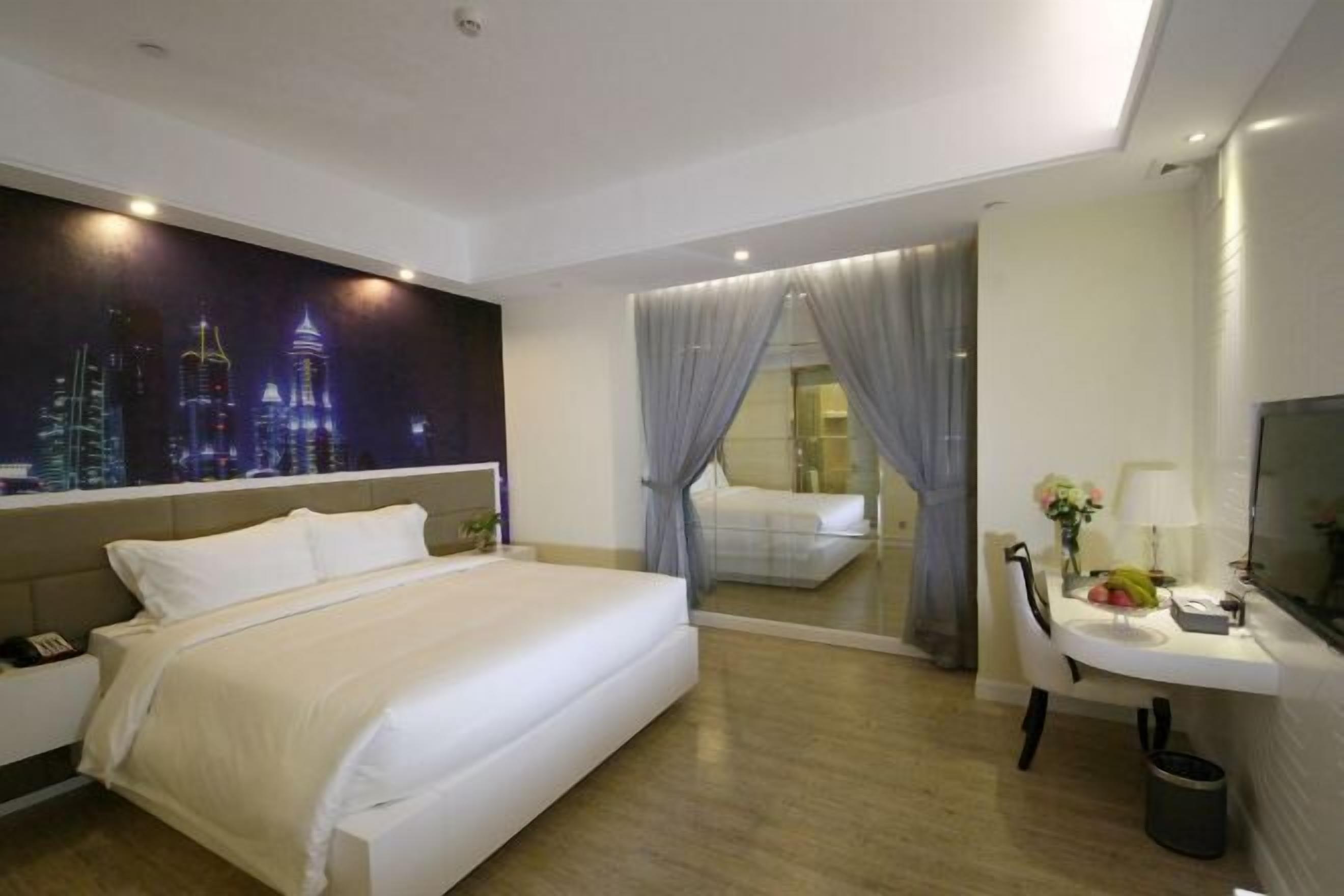 Quarto de hotel com cama, escrivaninha, cadeira, televisão e um mural com vista para a cidade.