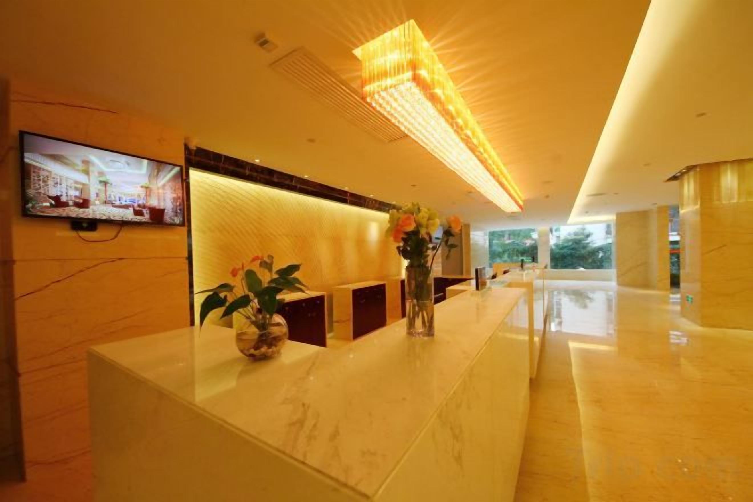 A hotel reception area with a marble counter, a flat-screen TV, and a large, illuminated ceiling light fixture.