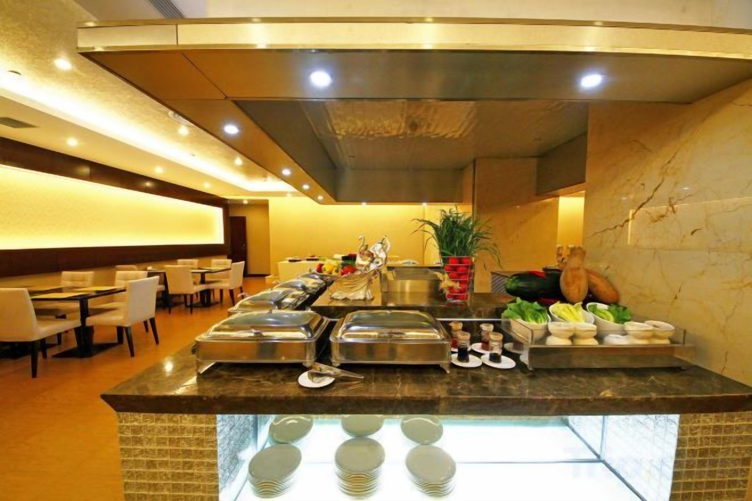 Espaço de buffet com estações de comida, assentos e uma planta.