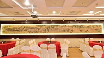 Un salón de conferencias con mesas redondas, sillas blancas y un cuadro grande colgado en la pared.