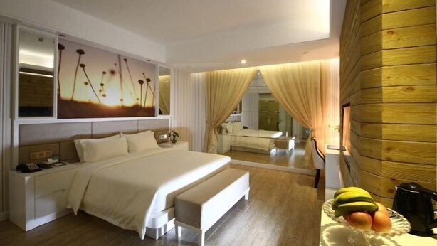 A modern hotel room with a large bed, a bedside table with a phone, a mirror, and a fruit bowl on the side table. - Huajun Hotel (Xiamen)