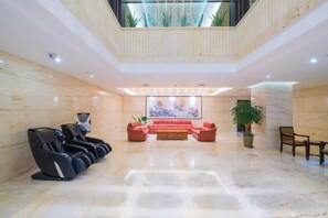 A lobby with a reception desk, massage chairs, a red sofa, and a large painting. - Huajun Hotel (Xiamen)