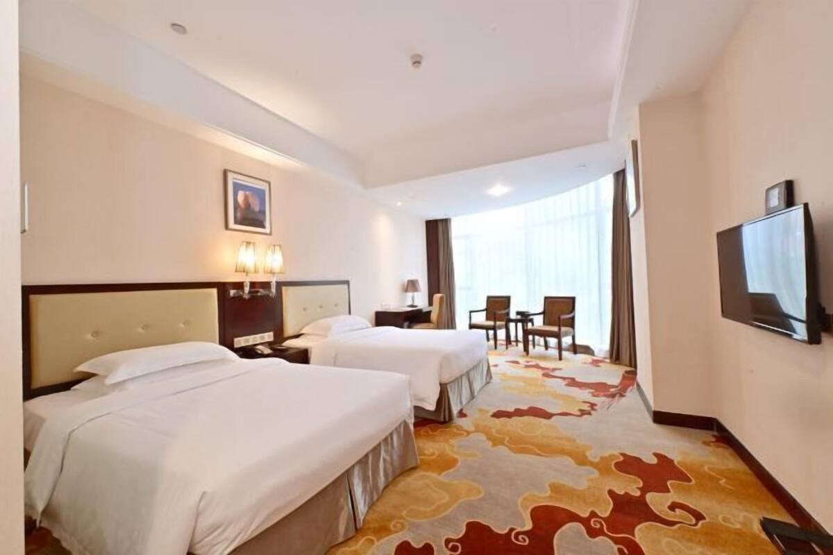 A hotel room with two beds, a television, a desk, and a chair.