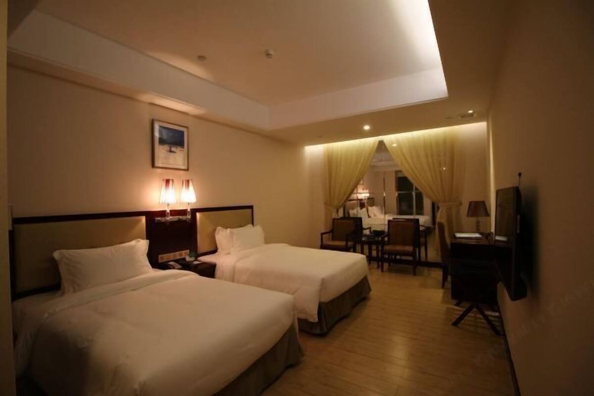 A hotel room with two beds, a desk, a chair, and a television.