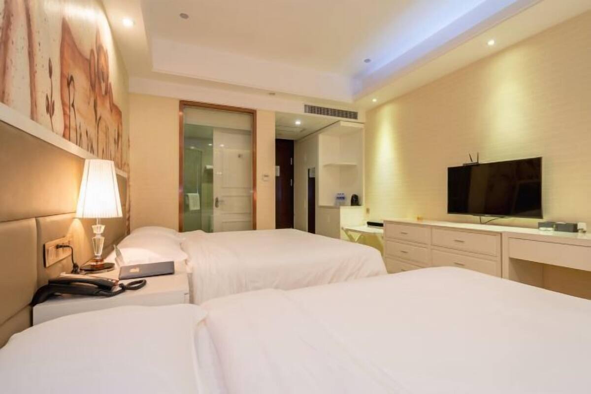 A hotel room with two beds, a desk, a television, and a mirror.