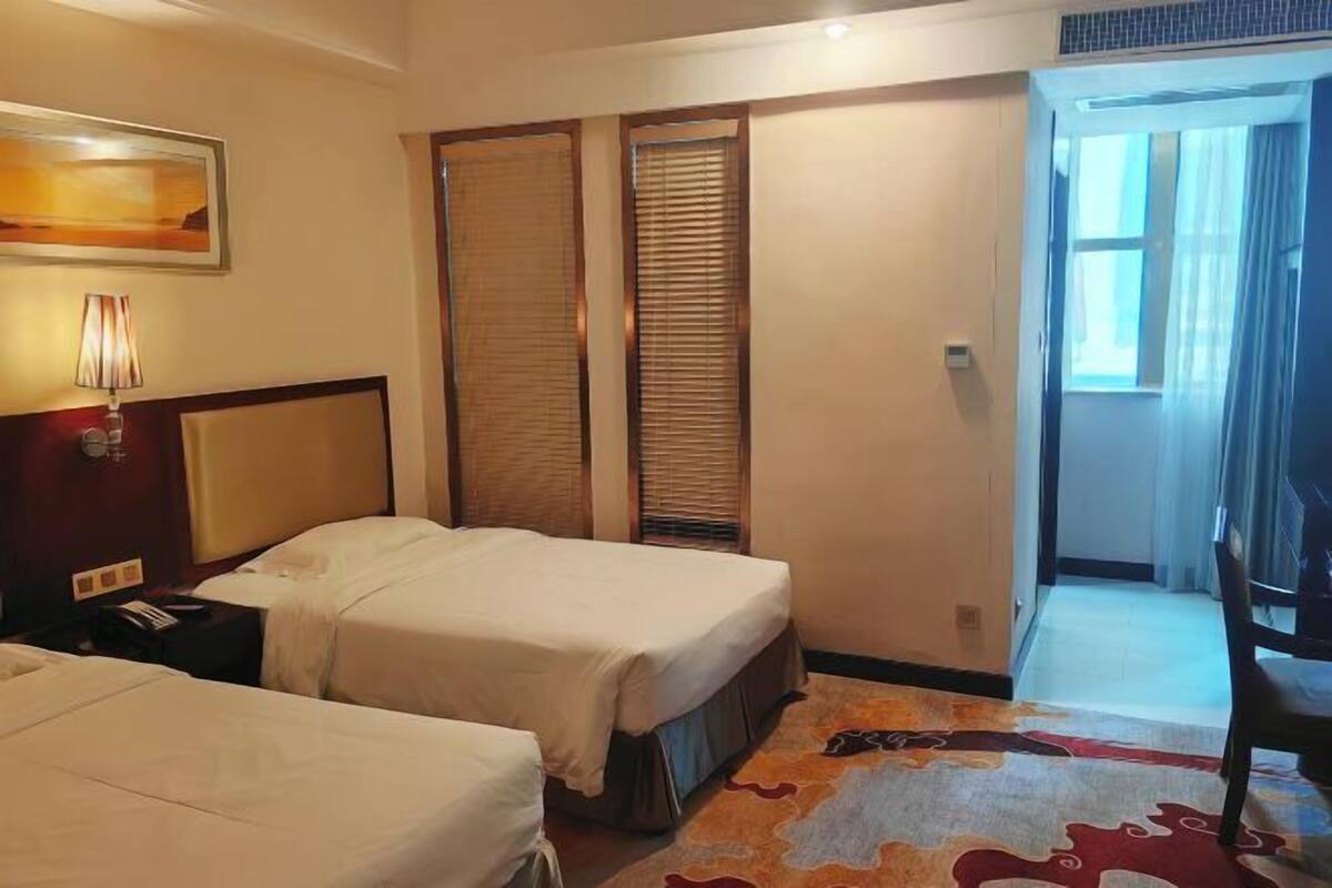 A hotel room with two beds, a nightstand, a lamp, and a door leading to a balcony.