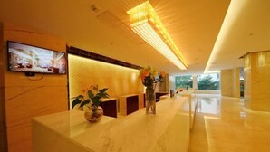 A modern hotel reception area with a marble counter, a television mounted on the wall, and a large, illuminated ceiling fixture. - Huajun Hotel (Xiamen)