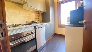Cocina compacta con estufa a gas, horno y lavavajillas, armarios de madera y ventana que proporciona luz natural.