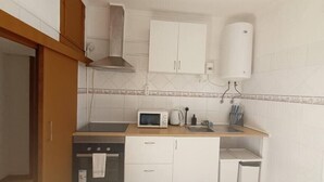 Una cuina compacta amb armaris blancs, microones, fogó i un rentapeus.