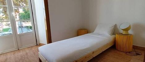 A bedroom with a wooden bed, a small bedside table with a lamp, and a sliding glass door leading to an outdoor area.