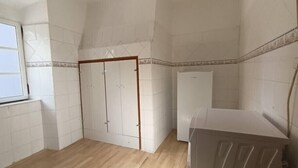 Una habitació amb parets revestides de rajoles blanques, sòl de fusta, un armari i una rentadora.