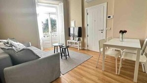 Un salon comprenant un canapé, un téléviseur, une table à manger avec des chaises et une porte-fenêtre donnant sur un balcon.