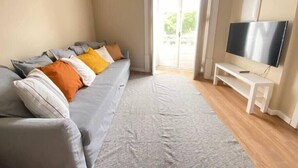 Un salon avec un canapé gris, un téléviseur à écran plat et une porte-fenêtre coulissante donnant sur un espace extérieur.