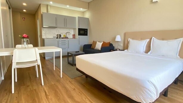 A hotel room with a large bed, a desk, a chair, a sofa, and a kitchenette in the background. - Setúbal Prime III (Setúbal)