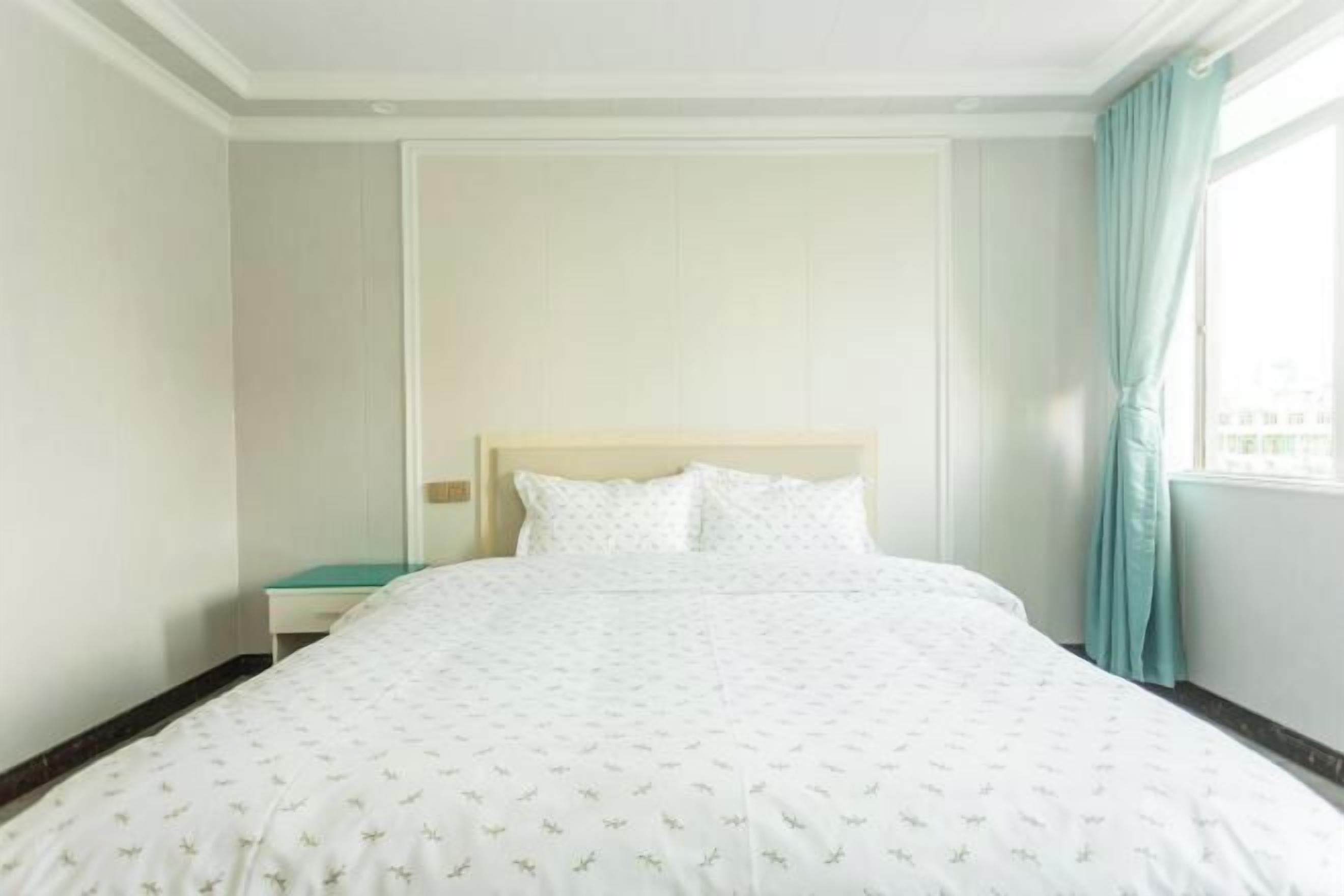 A hotel room with a large bed, a nightstand, and a window with curtains.