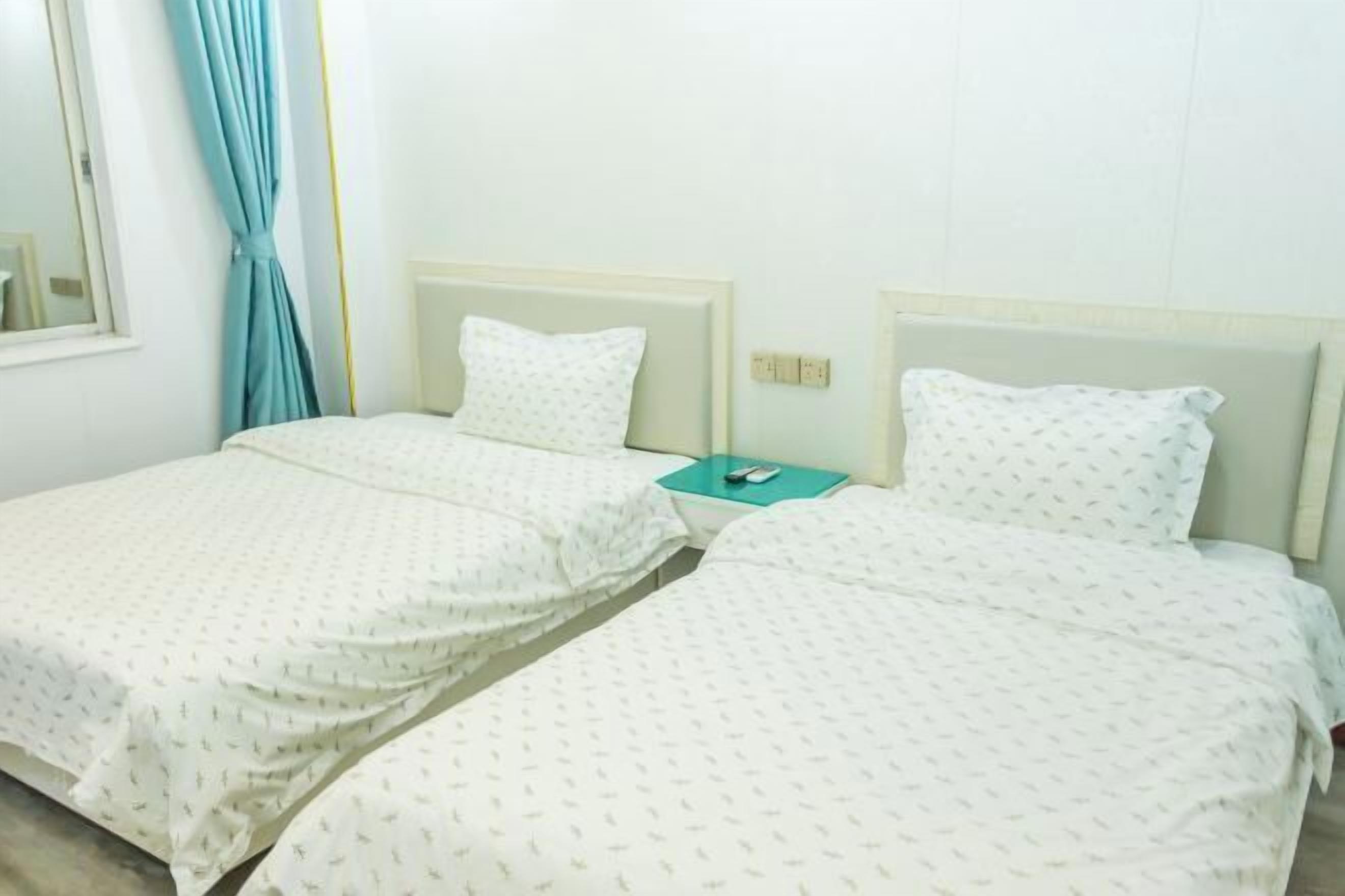A hotel room with two single beds, each with a white bedspread and matching pillow. There is a small table between the beds with a remote control on it.